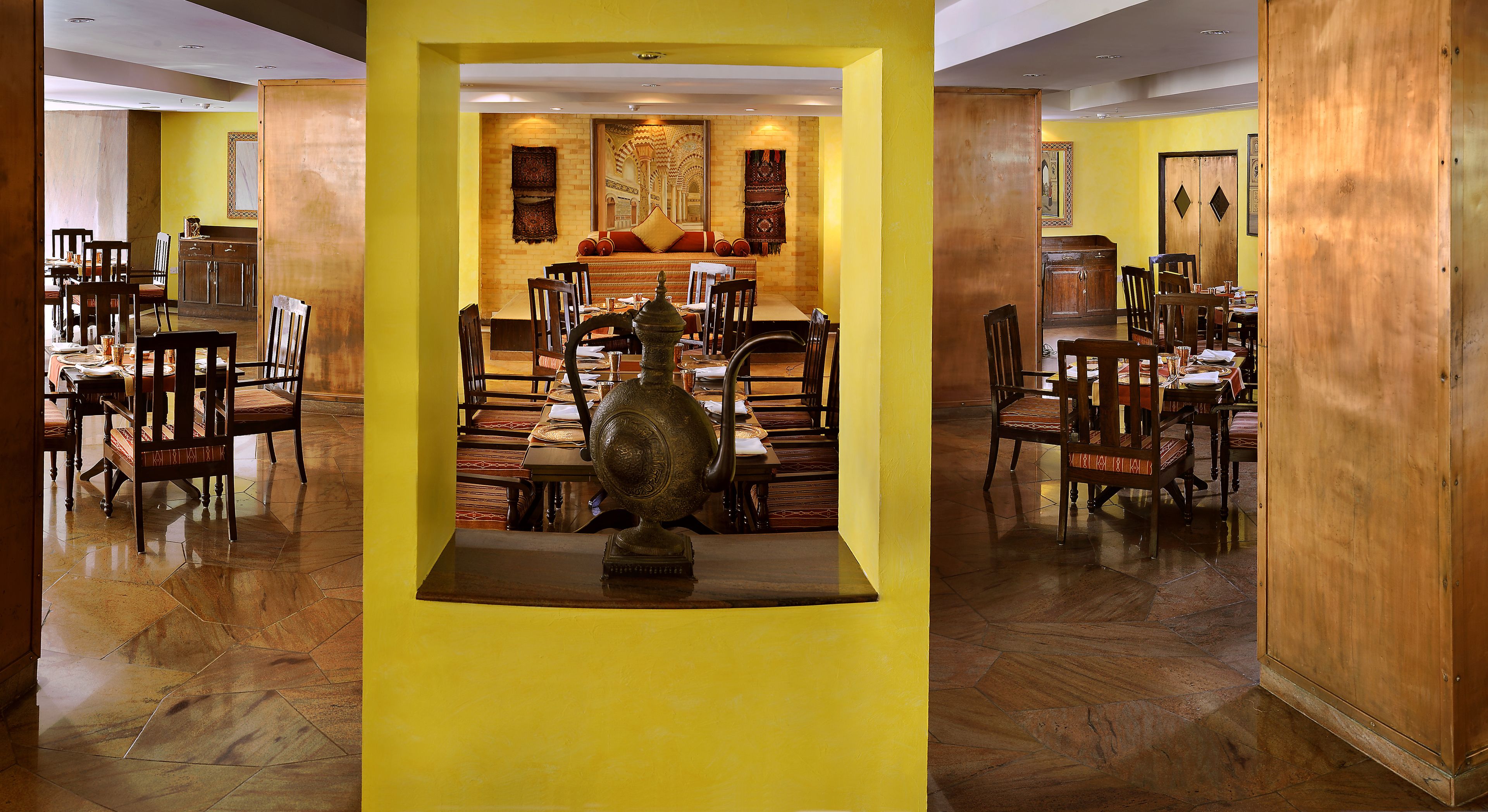 Un comedor con varias mesas y sillas, una pieza decorativa central y una pared de color amarillo.