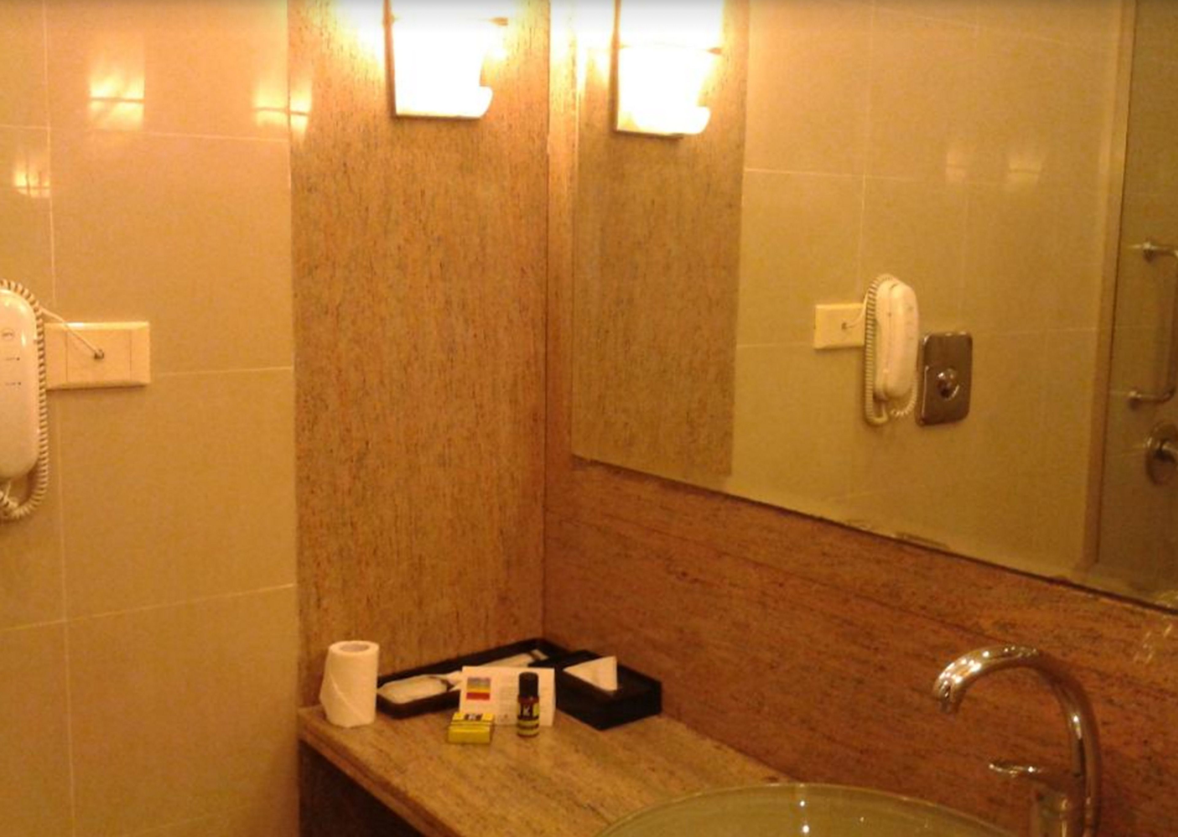 Un baño con lavamanos, espejo y dos teléfonos. Hay artículos de aseo en la encimera.