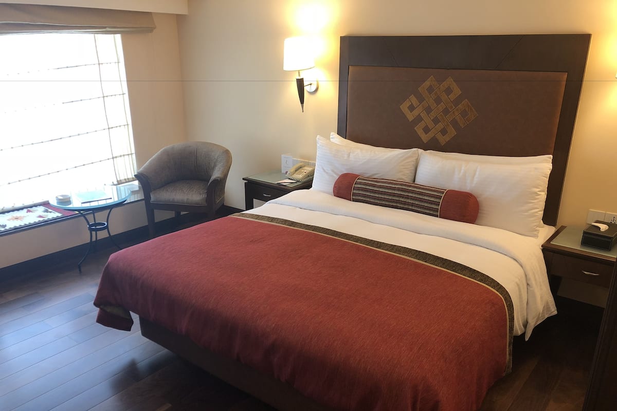 Quarto de hotel com uma cama grande, uma cadeira, mesa de cabeceira com abajur e janela com persianas.