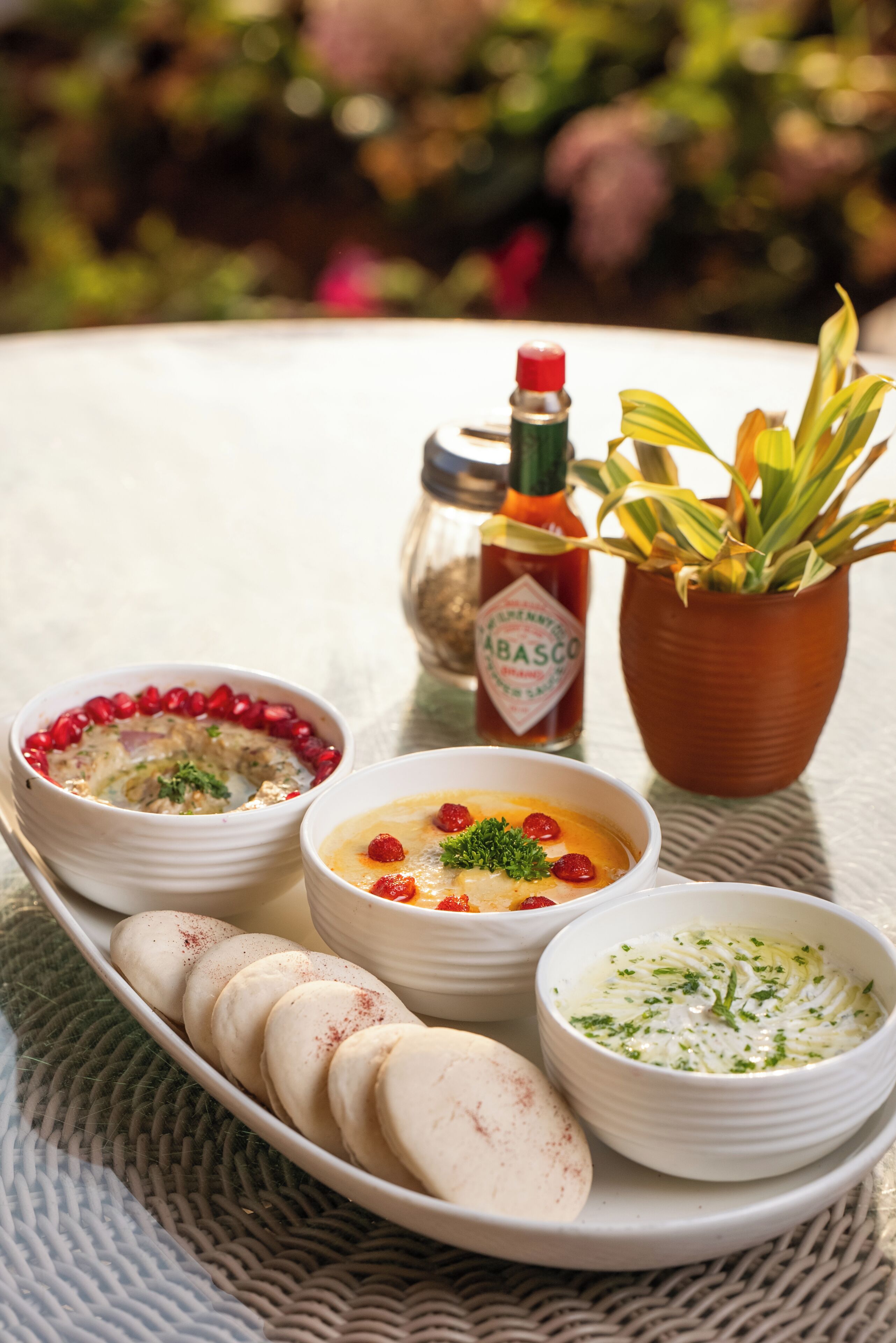 Una mesa servida con varios platos, incluyendo tazones de sopa y una fuente de pan, una botella de salsa y una planta en maceta.