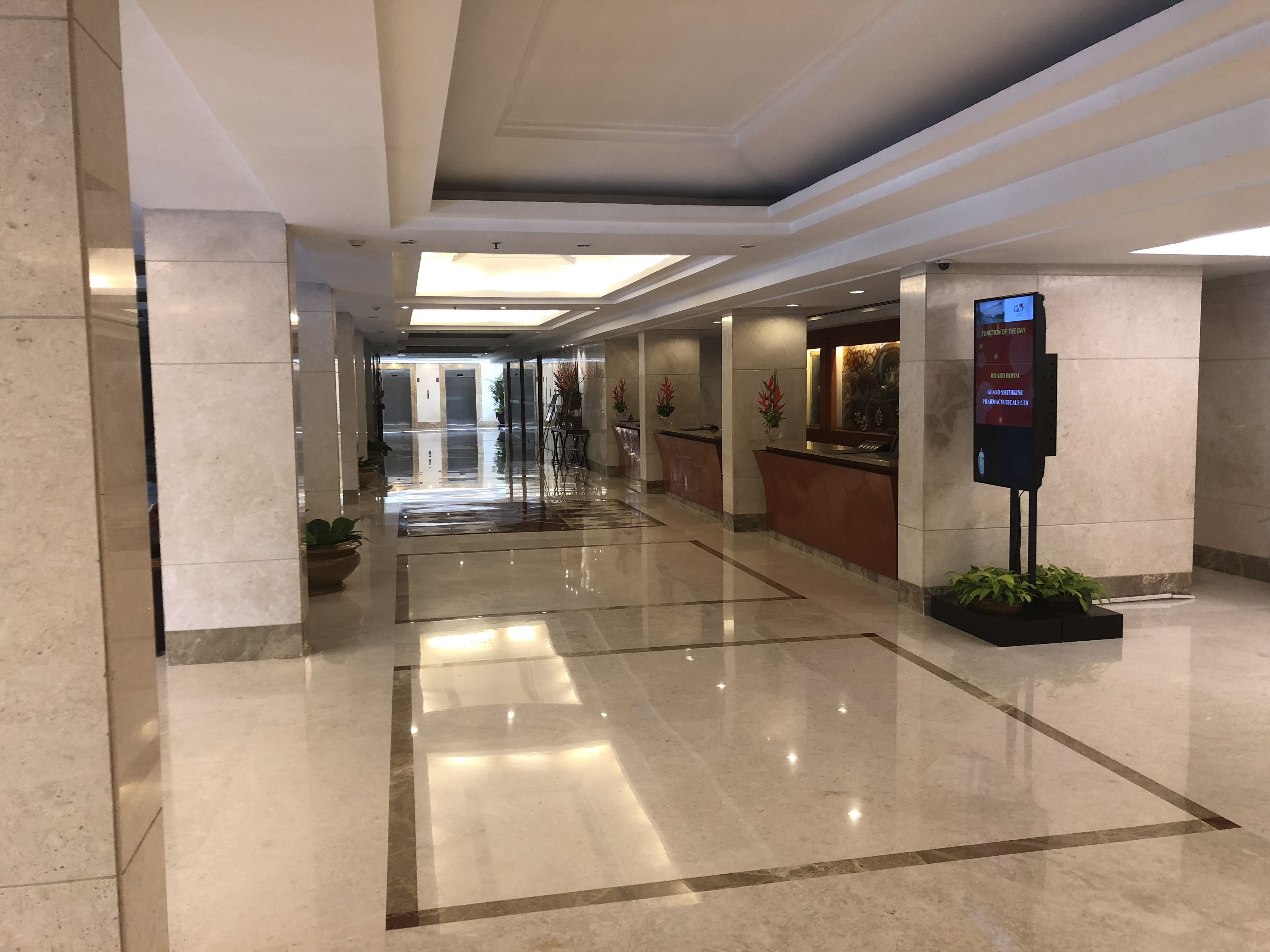 Un hall d’hôtel doté d’un sol en marbre poli, d’un comptoir d’accueil et d’un panneau d’affichage numérique.
