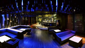 Un área de estar moderna con sofás y mesas, un bar al fondo y un diseño de techo original.