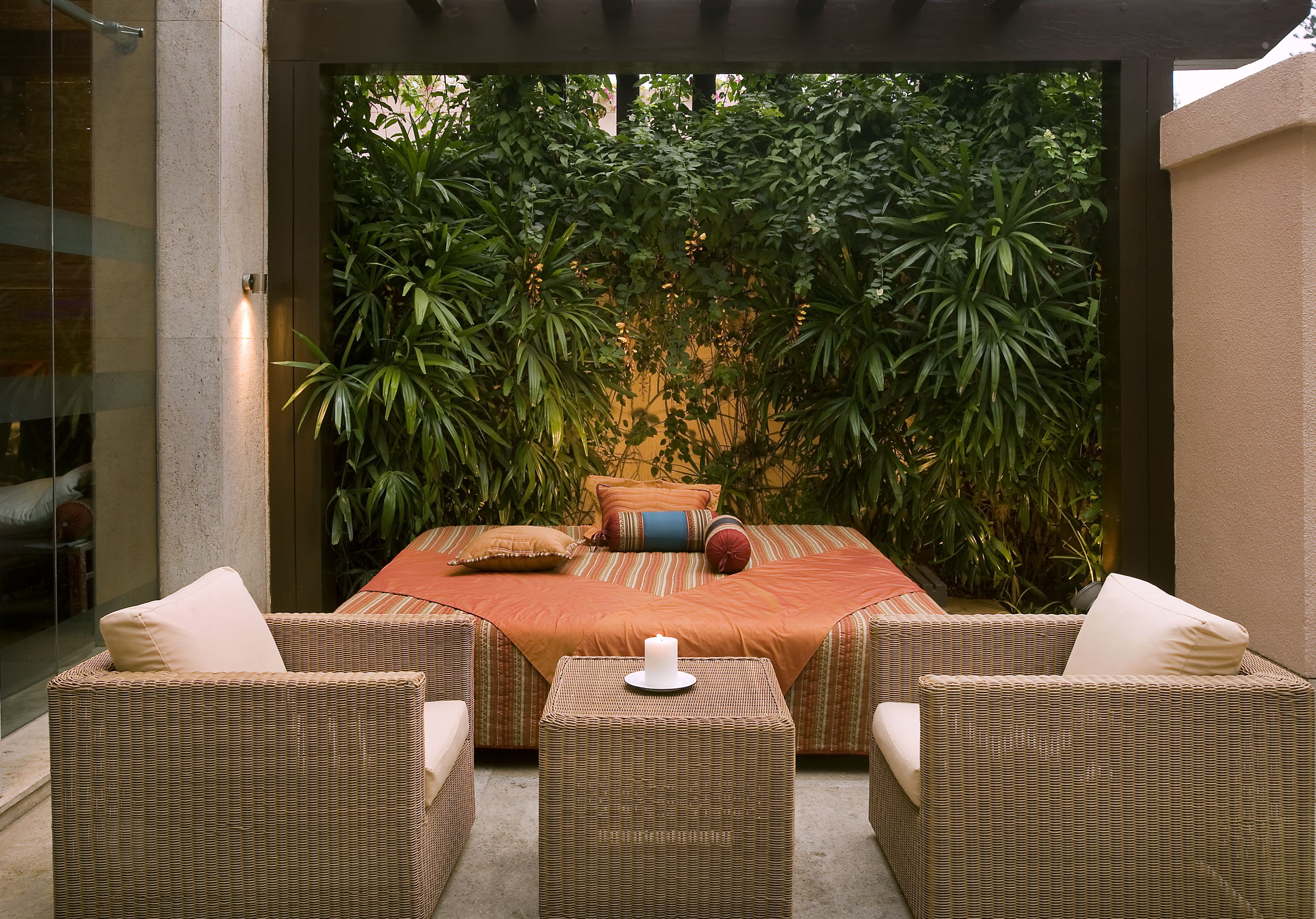 Un rincón exterior acogedor con muebles de mimbre y una cama con colcha naranja.