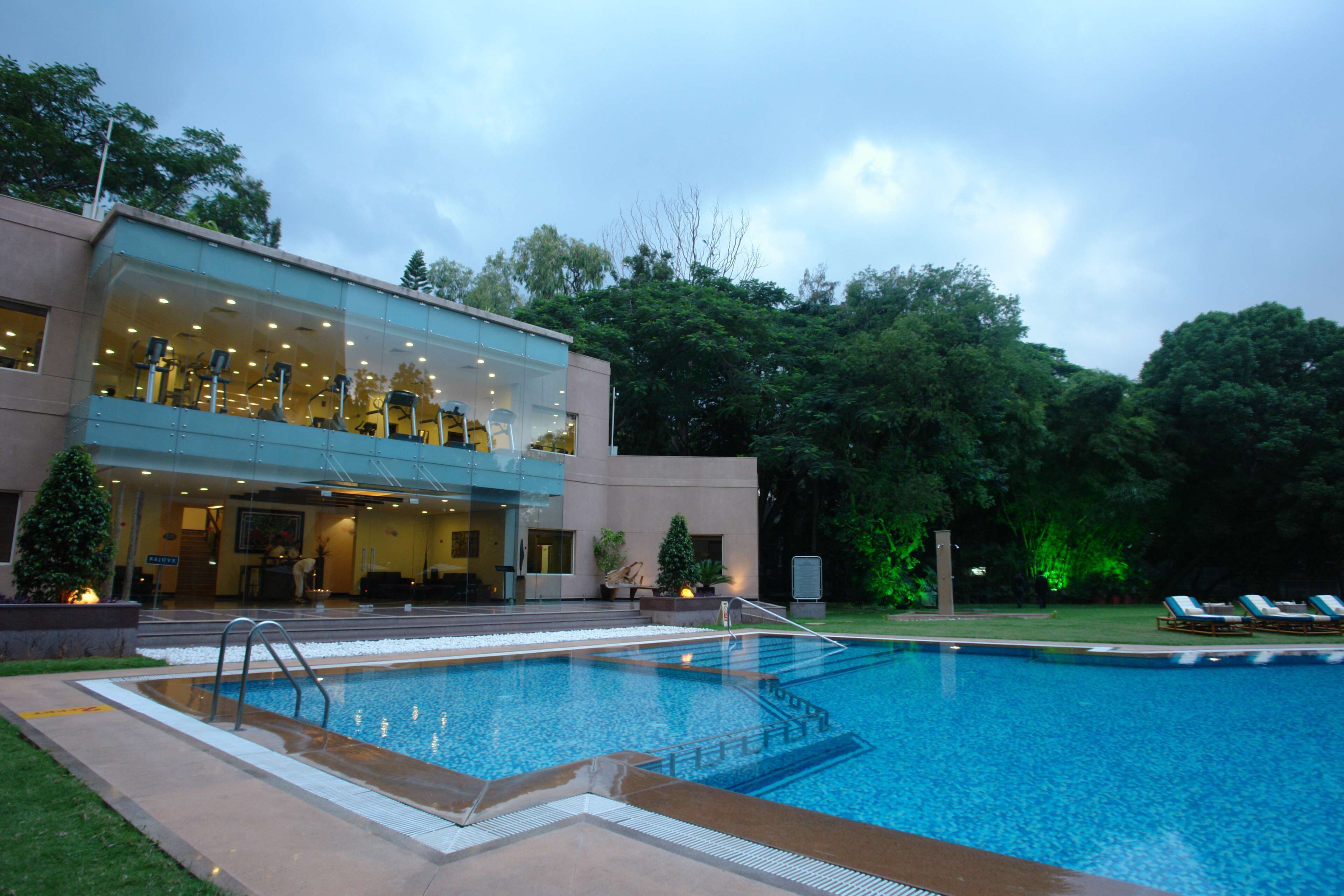 A modern hotel with a glass facade, a swimming pool, and outdoor seating.