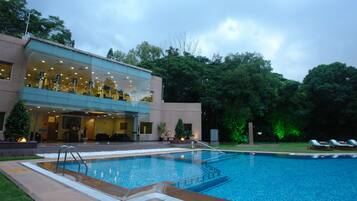 A modern hotel with a glass facade, a swimming pool, and outdoor seating.