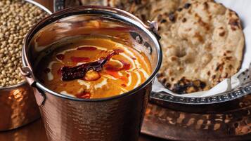 A copper cup with a creamy beverage, a plate of flatbread, and a bowl of lentils.