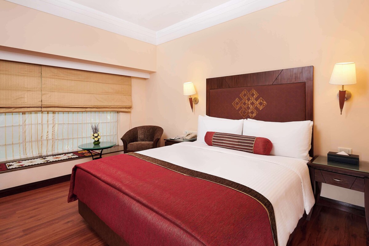 A hotel room with a large bed, a chair, a bedside table, and a lamp.