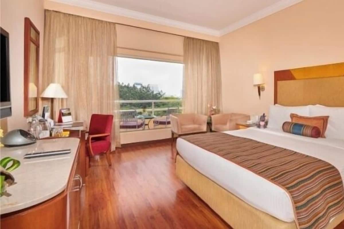 Quarto de hotel com uma cama grande, uma mesa com computador, uma cadeira e vista para o exterior.