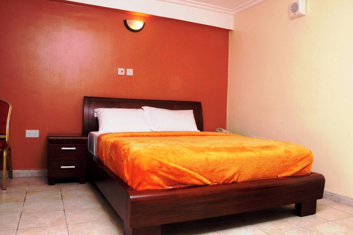 A bedroom with a wooden bed, a nightstand, and a wall-mounted light fixture.