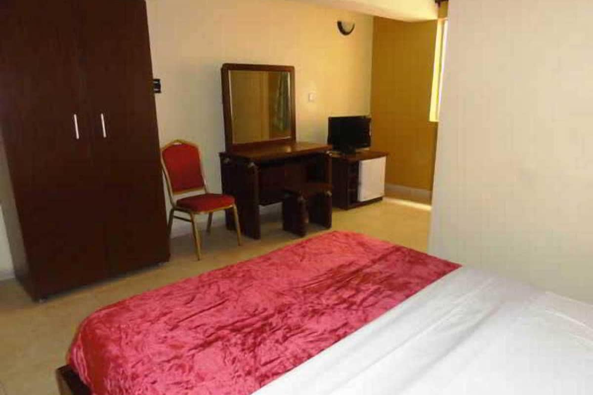 A bedroom with a bed, a desk, a chair, a wardrobe, and a television.