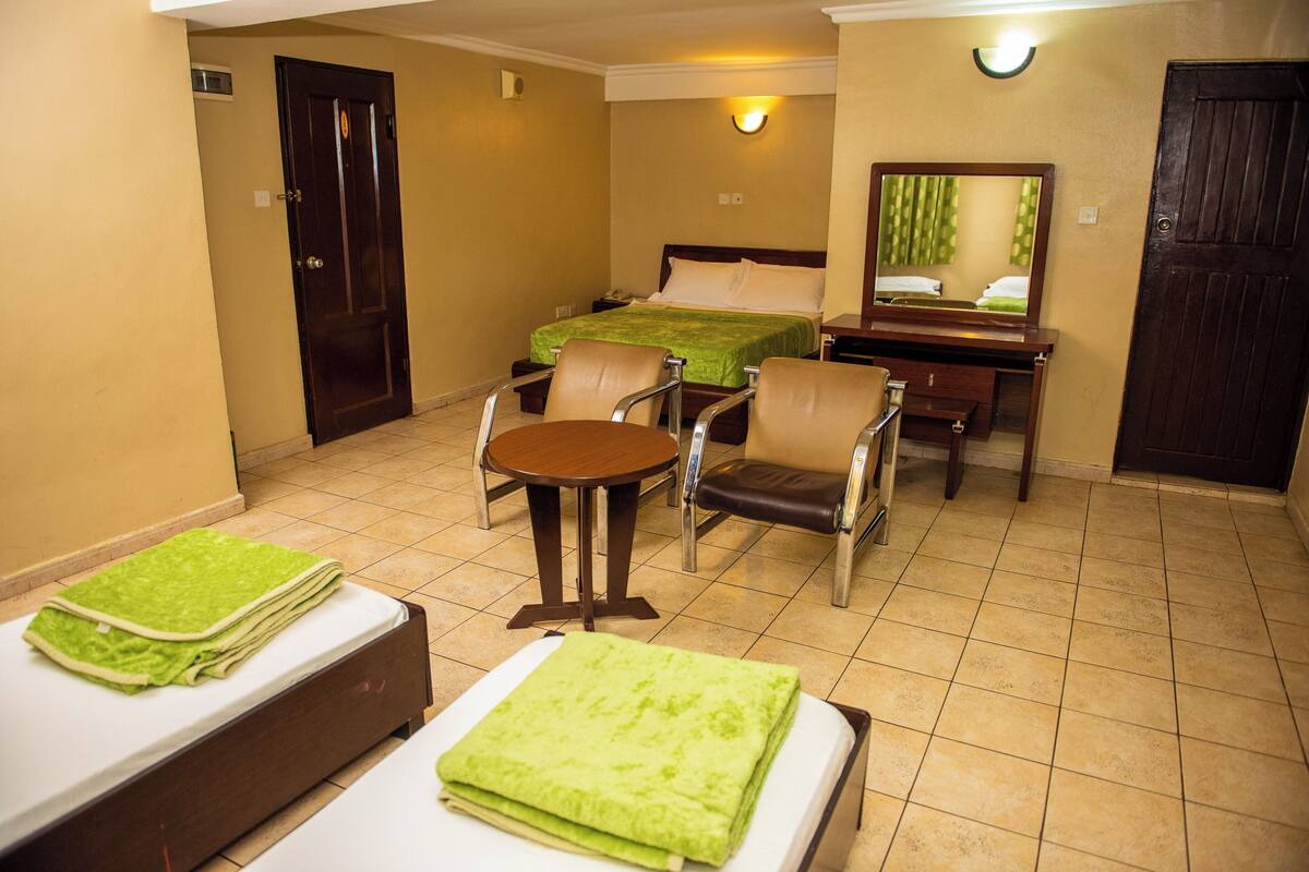 A hotel room with a bed, a desk, a chair, a table, and a mirror.