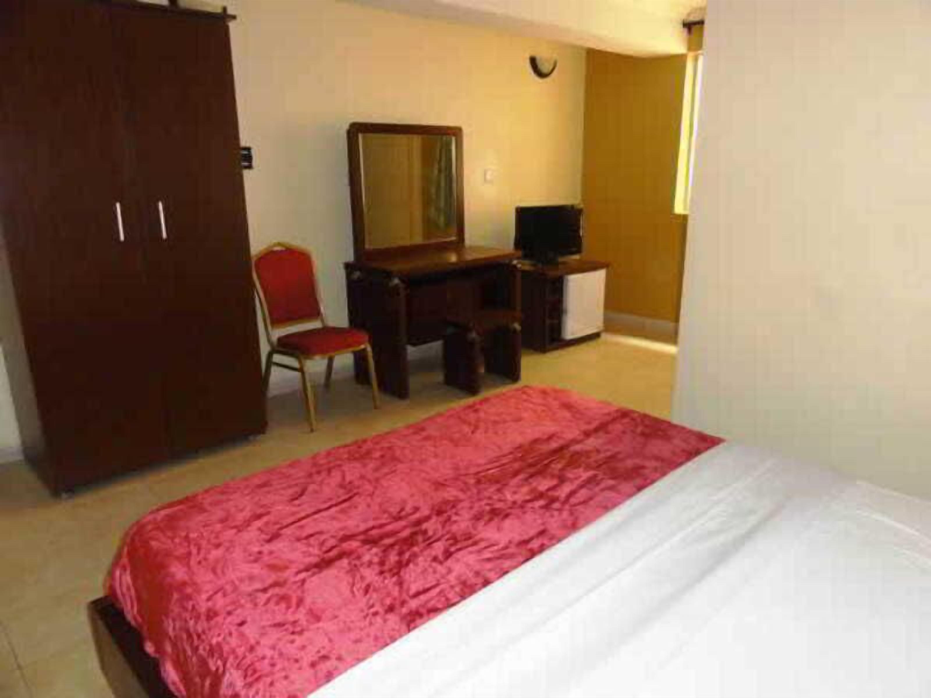 A bedroom with a bed, a desk, a chair, a wardrobe, and a television.