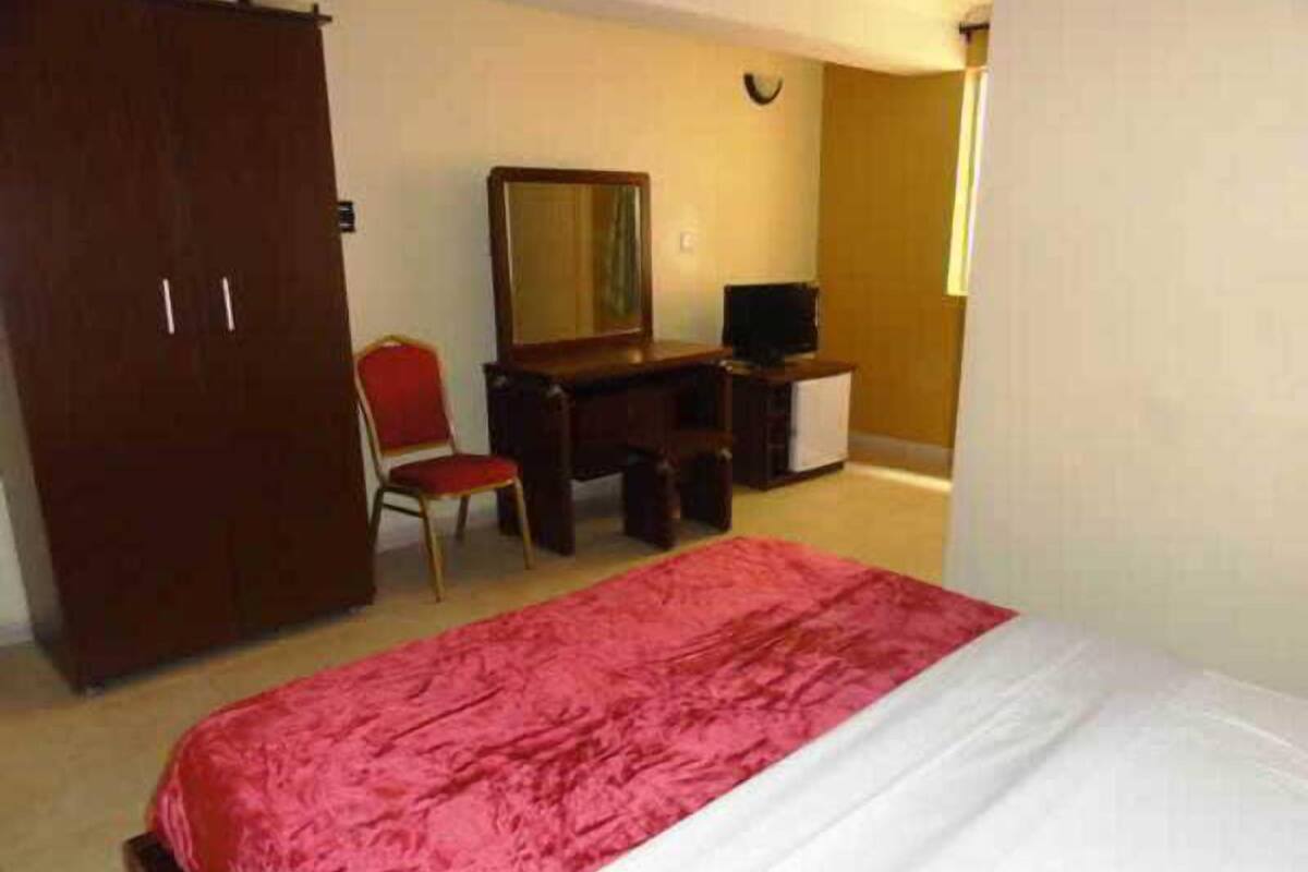 A bedroom with a bed, a desk, a chair, a wardrobe, and a television.