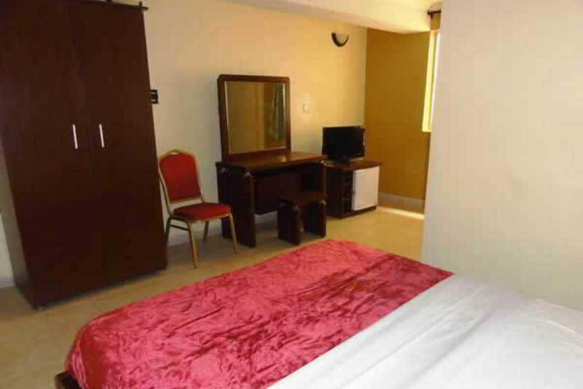 Un dormitorio con cama, escritorio, silla, armario y televisor.