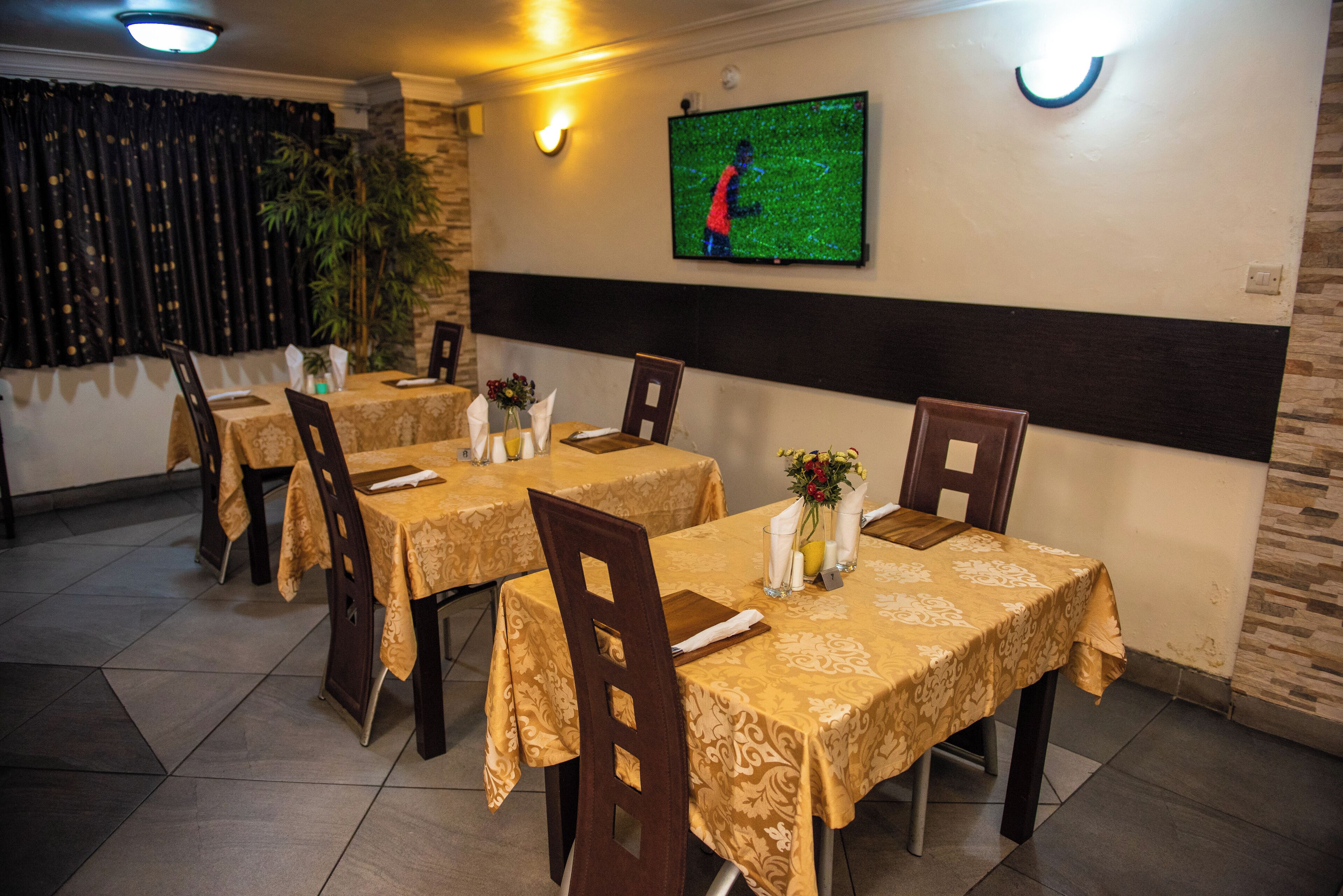 Un restaurant amb taules cobertes amb camases grogues, cadires de fusta i un televisor de pantalla plana penjat a la pared.
