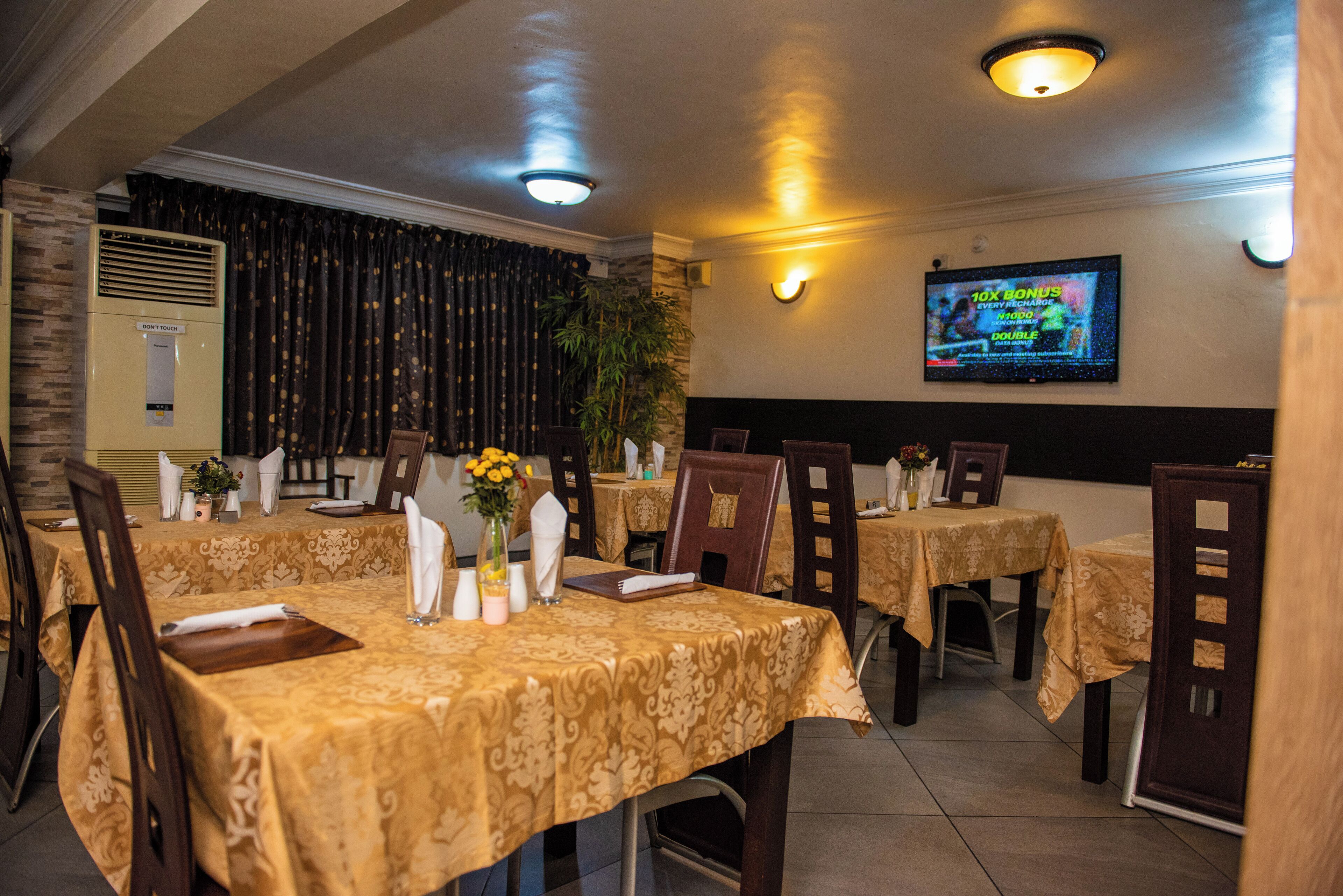 Un restaurante con mesas cubiertas de manteles dorados, sillas y una pantalla de televisión que muestra un partido.