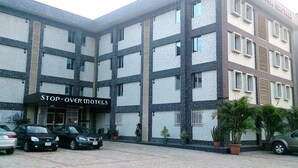A multi-story building with a sign reading "STOP-OVER MOTELS". There are several cars parked in front, and potted plants are placed along the building's facade. - Stop Over Motels (Lagos)
