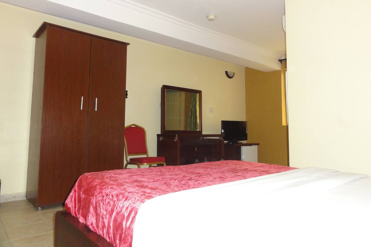 A bedroom with a bed, a wardrobe, a desk with a computer, and a chair.