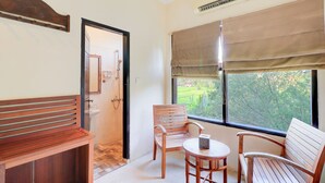 A room with a wooden bench, two chairs, a small table, and a window with a view of greenery. - Collection O Ubud Near Central Ubud Formerly Hotel Suly (Ubud)