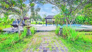 A pool area with a stone pathway leading to a seating area, surrounded by lush greenery and trees. - Collection O Ubud Near Central Ubud Formerly Hotel Suly (Ubud)