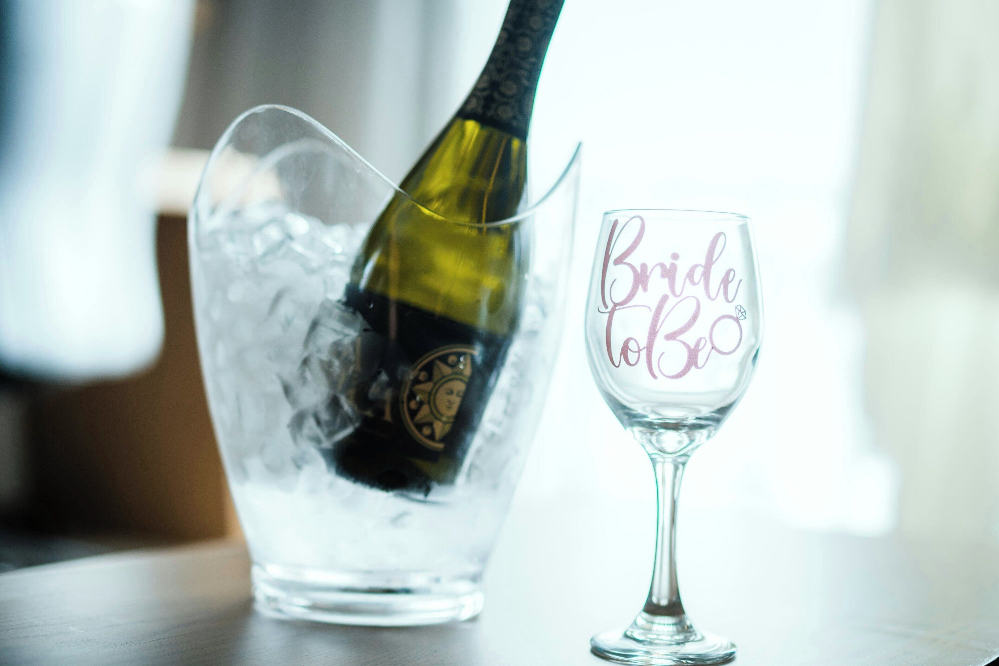 A bottle of champagne being poured into a glass with "Bride to Be" written on it.