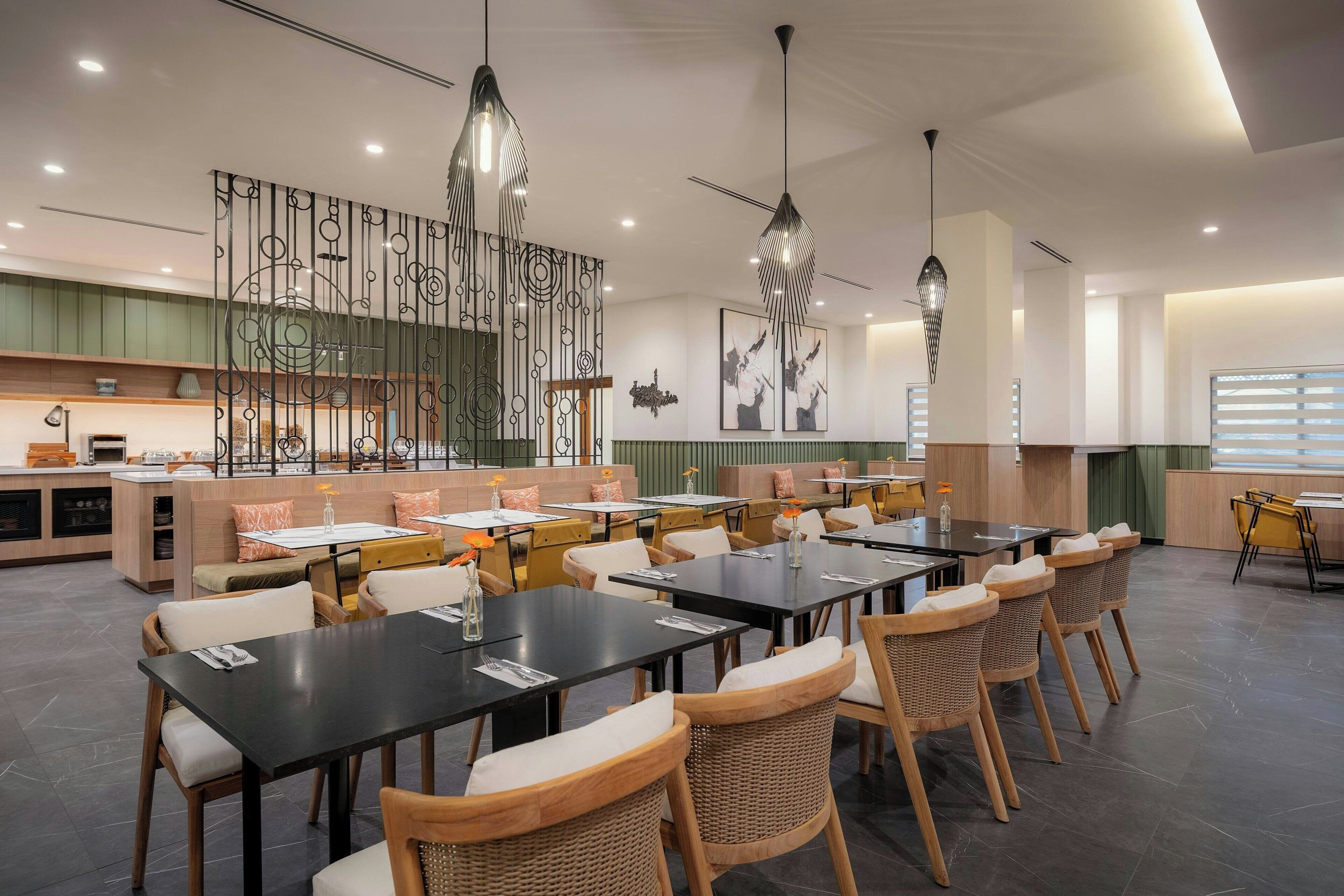 A modern restaurant with multiple dining tables and chairs, a decorative wall, and pendant lighting.