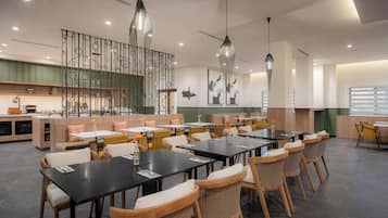 A modern restaurant with multiple dining tables and chairs, a decorative wall, and pendant lighting.