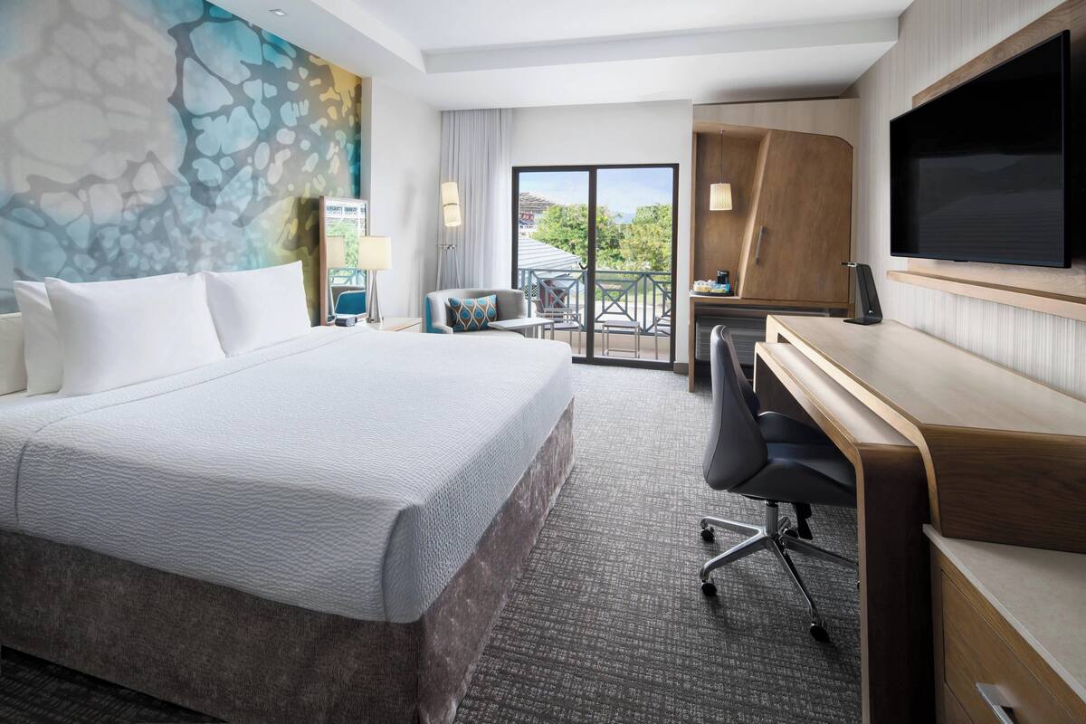 Habitación de hotel con una cama grande, un escritorio, un televisor de pantalla plana y un balcón con vistas.