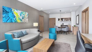 A modern living room with a grey sofa, blue armchairs, a wooden coffee table, and a kitchen in the background.
