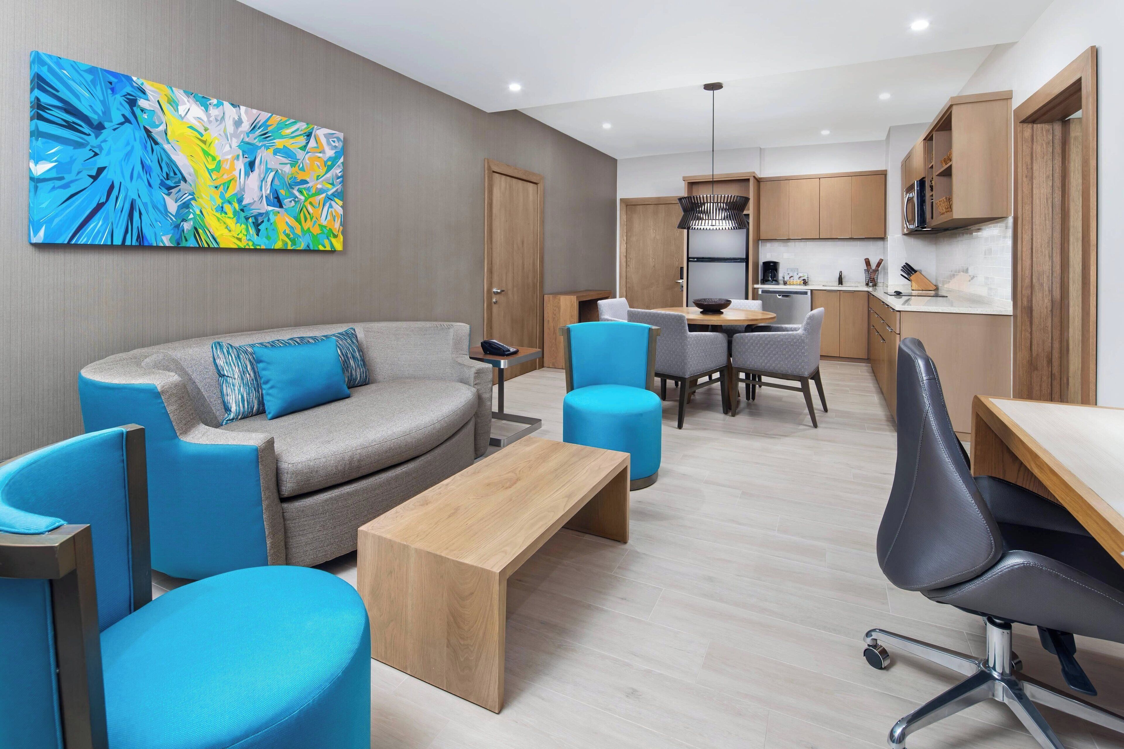 Una sala moderna con un sofá gris, sillones azules y una mesa de centro de madera.