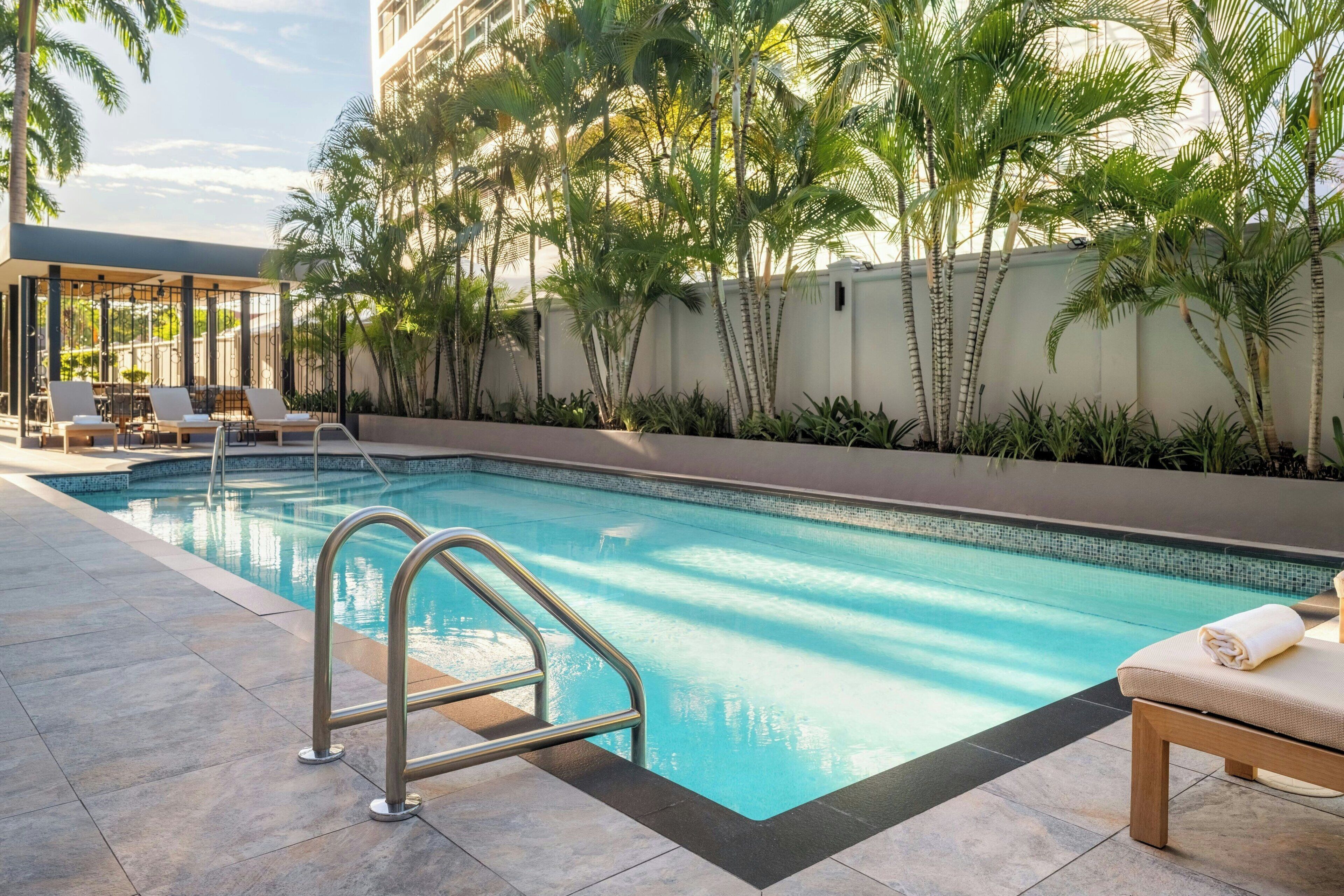 A swimming pool with lounge chairs and a covered seating area, surrounded by palm trees.