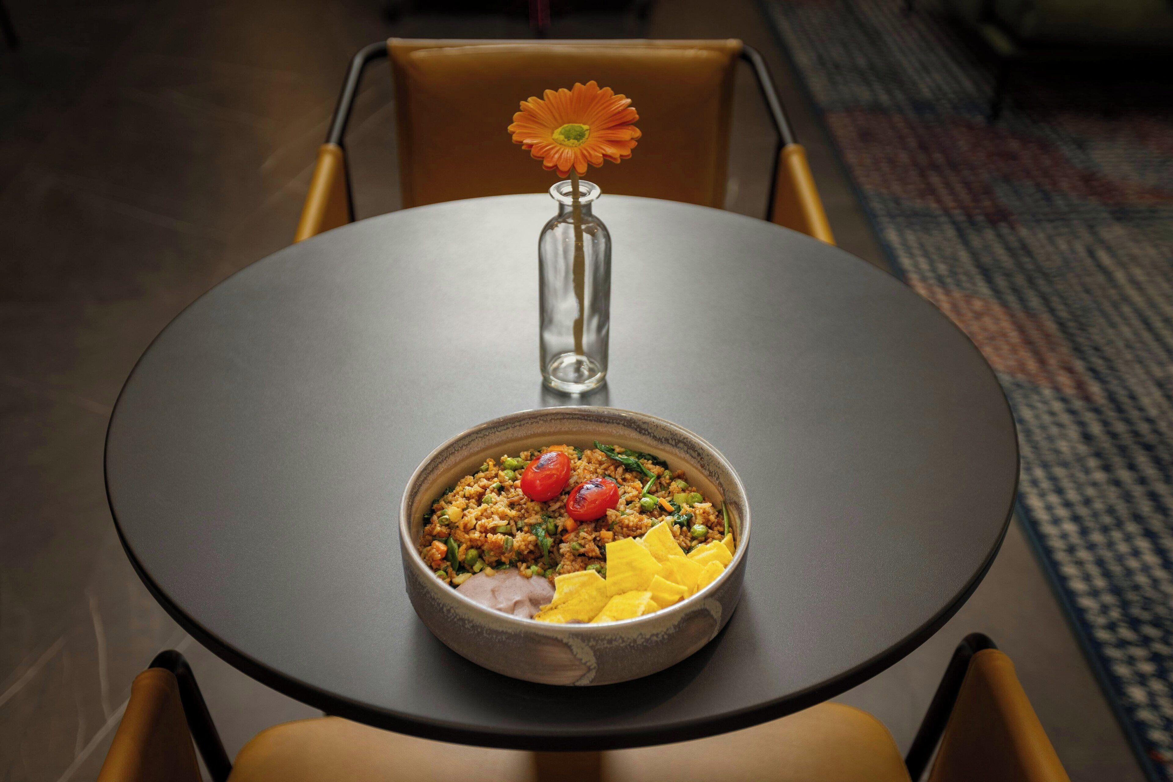 A dining table with a bowl of food and a vase with a single flower.