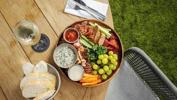 A wooden table with a charcuterie board, a glass of white wine, and a wicker chair.
