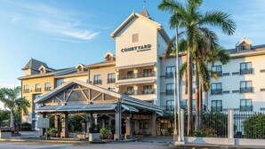 Un hotel Courtyard by Marriott con entrada techada, varios balcones y palmeras.