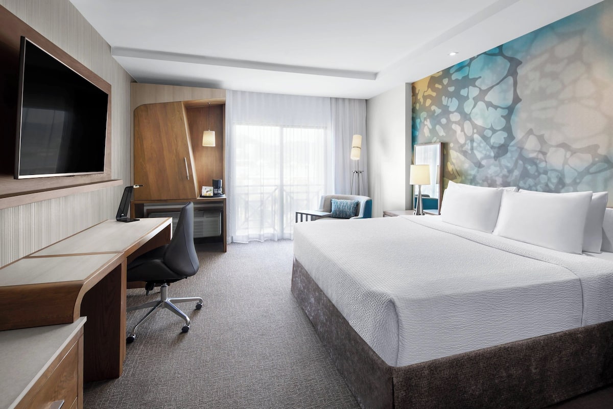 Una habitación de hotel con una cama grande, un escritorio con silla, un televisor y un cuadro en la pared.