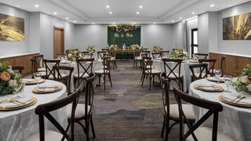 A banquet hall with round tables, each set with white tablecloths, gold-rimmed plates, and floral centerpieces.