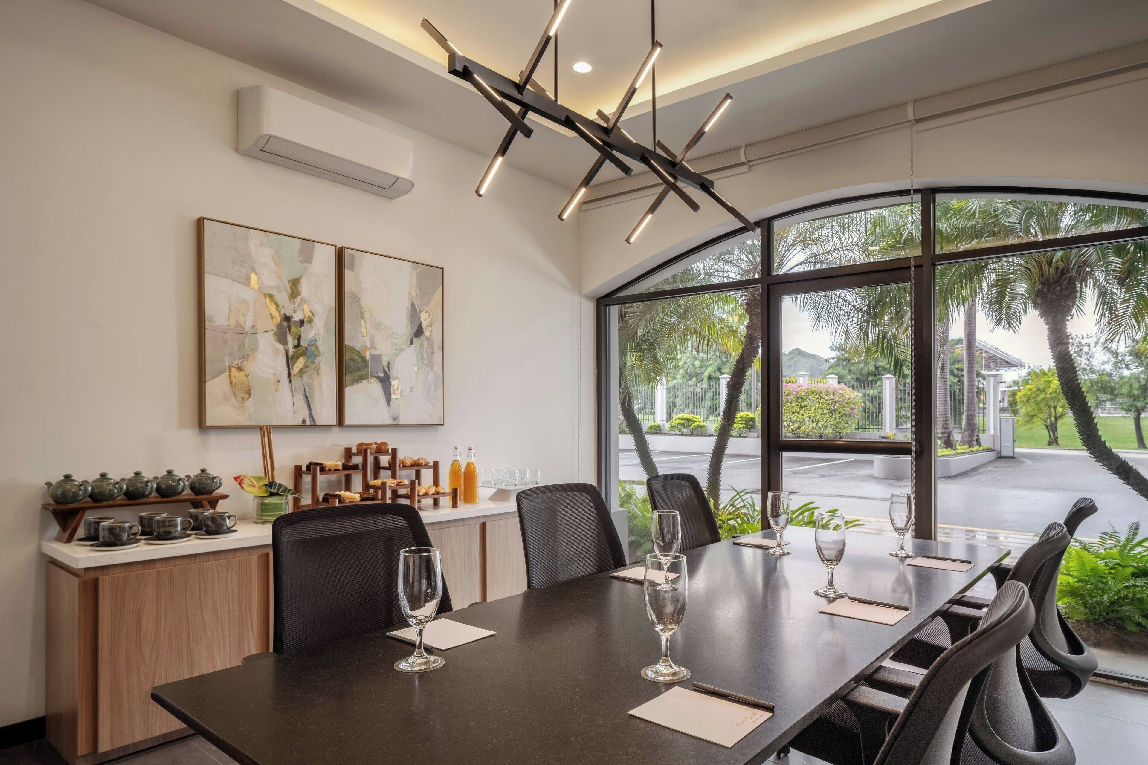 A modern conference room with a large table, chairs, and a view of palm trees through large windows.