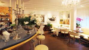 A bar area with a bar counter, stools, and a chandelier. There are tables and chairs in the dining area, and a large window with curtains. - Hotel Sommerau-Ticino (Dietikon)