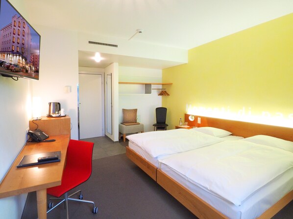 A hotel room with a bed, a desk with a laptop, a chair, a bedside table with a lamp, and a television on the wall. - Hotel Sommerau-Ticino (Dietikon)