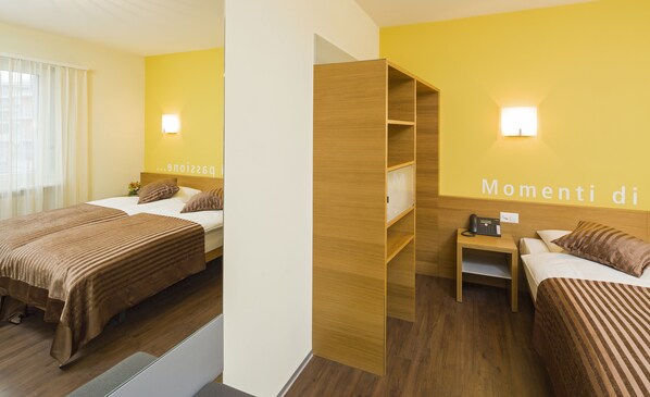 A hotel room with two beds, a wooden wardrobe, a bedside table with a phone, and a wall with a light fixture. - Hotel Sommerau-Ticino (Dietikon)