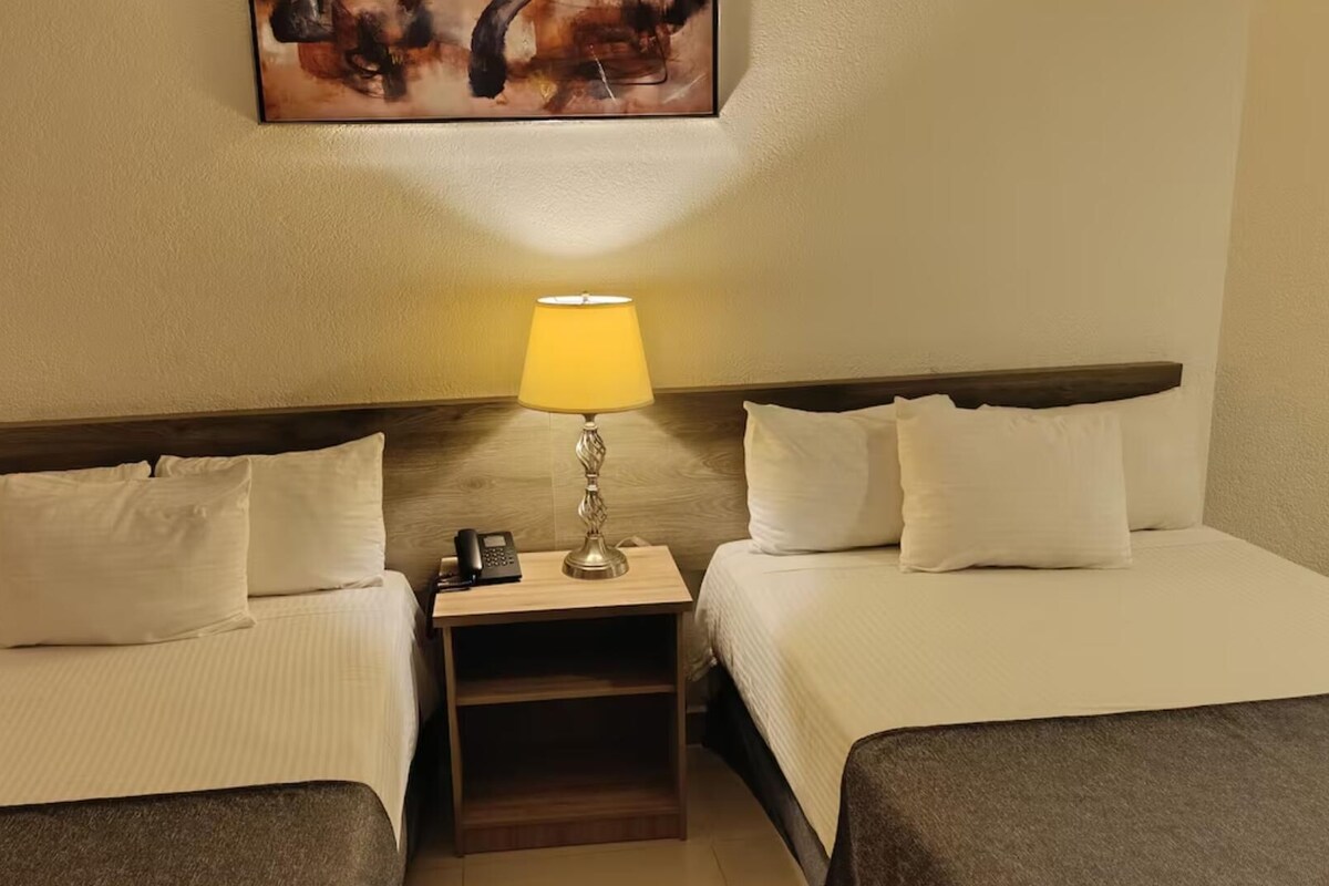 A hotel room with two beds, a nightstand with a lamp, a phone, and a painting on the wall.