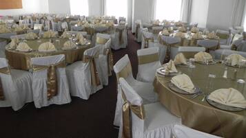 Een feestzaal met ronde tafels, bedekt met witte tafelkleden en gouden linten, gerangschikt in rijen.