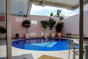A swimming pool with a clear blue water feature, surrounded by potted plants and lounge chairs.