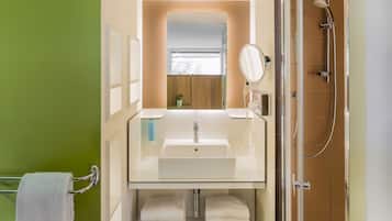 Een badkamer met een glazen wastafel, een spiegel, een handdoekhouder en een douche.