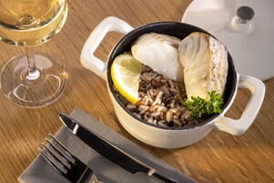 Una olla blanca con pescado y arroz sobre una mesa de madera.
