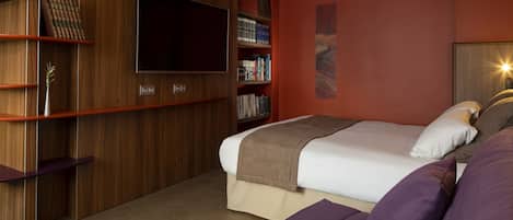 A bedroom with a bed, a TV, bookshelves, and a painting on the wall.
