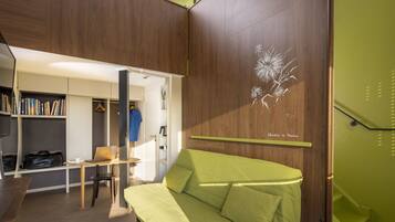 A modern room with a green sofa, a desk with a laptop, a bookshelf, and a wardrobe.
