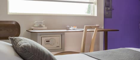 Een slaapkamer met een bed, een nachtkastje met een kopje en schotel, een stoel, een bureau met een computer, en een paarse deur.