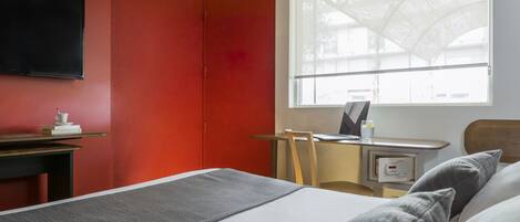 A hotel room with a bed, a desk, a chair, a TV, and a window with a view.