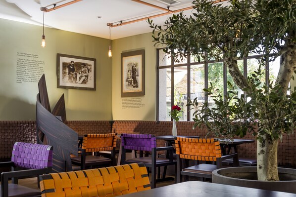 A restaurant interior with brick walls, framed artwork, and a large potted tree. - Terre de Provence Hôtel & Spa (Le Pontet)